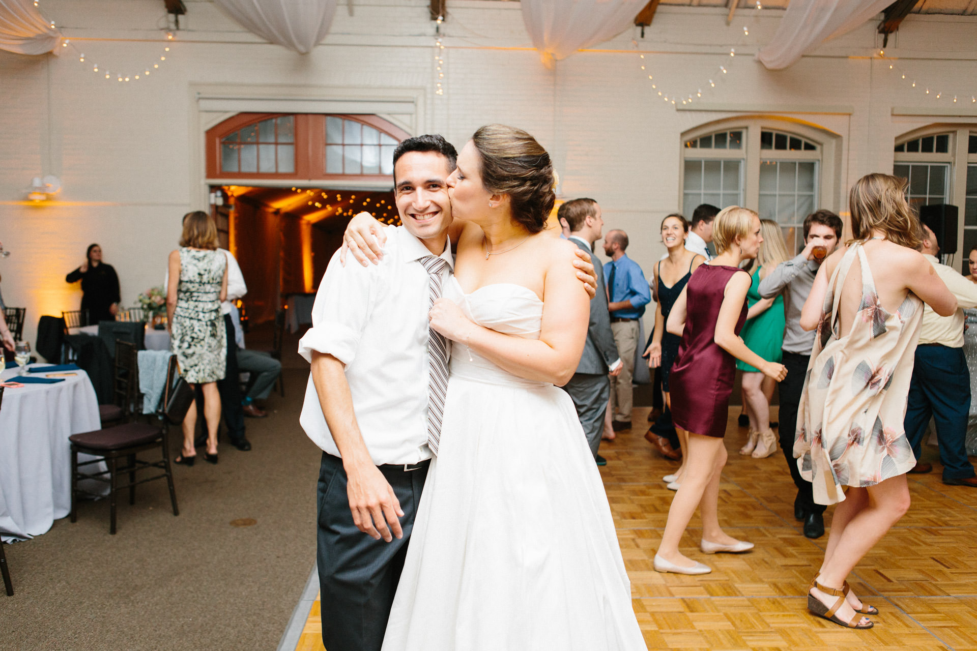 Bride kissing her brother while guests dance around them