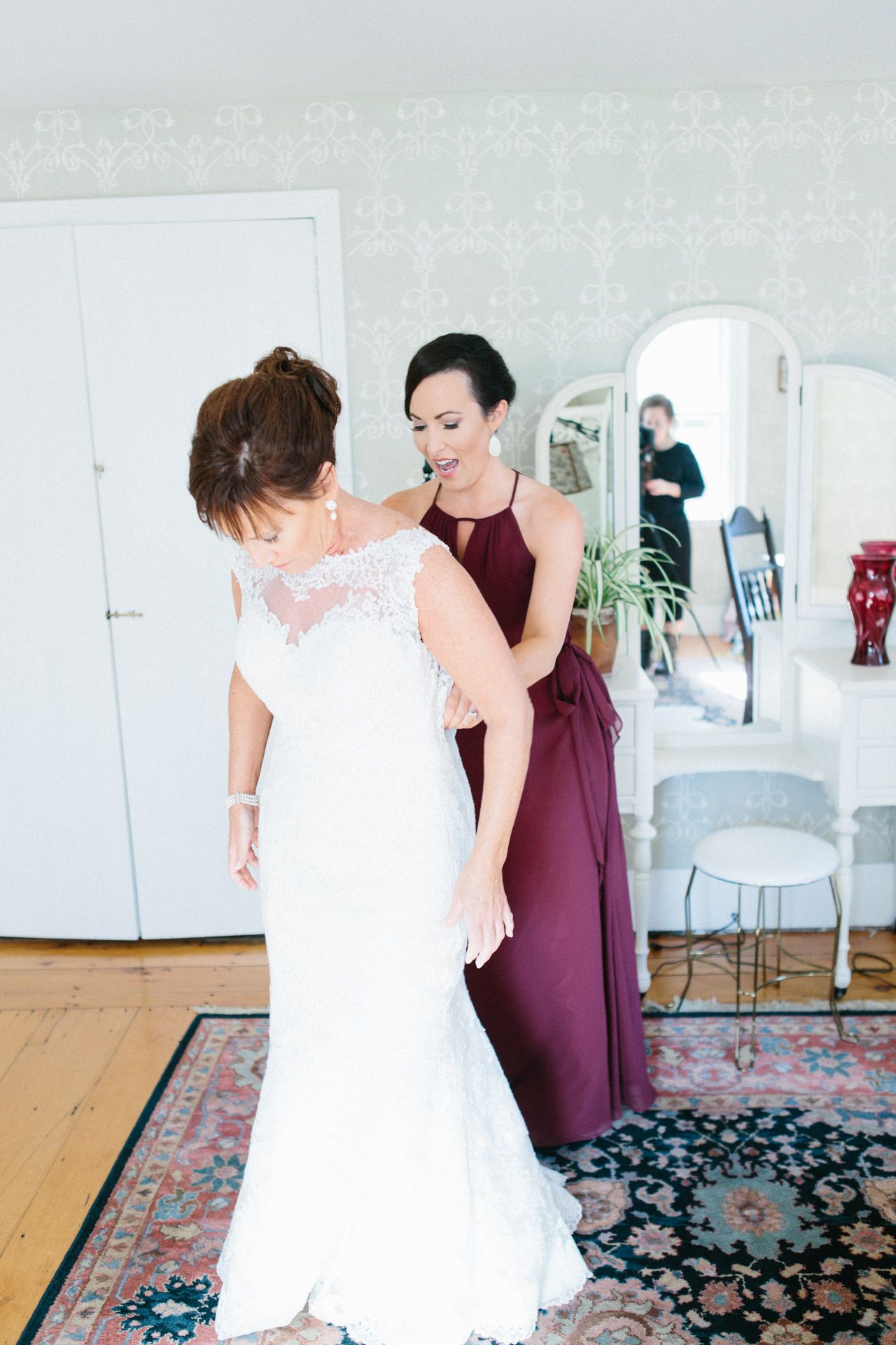 Bride's daughter helps bride into wedding gown before ceremony at Peirce Farm at Witch Hill wedding in Topsfield, MA