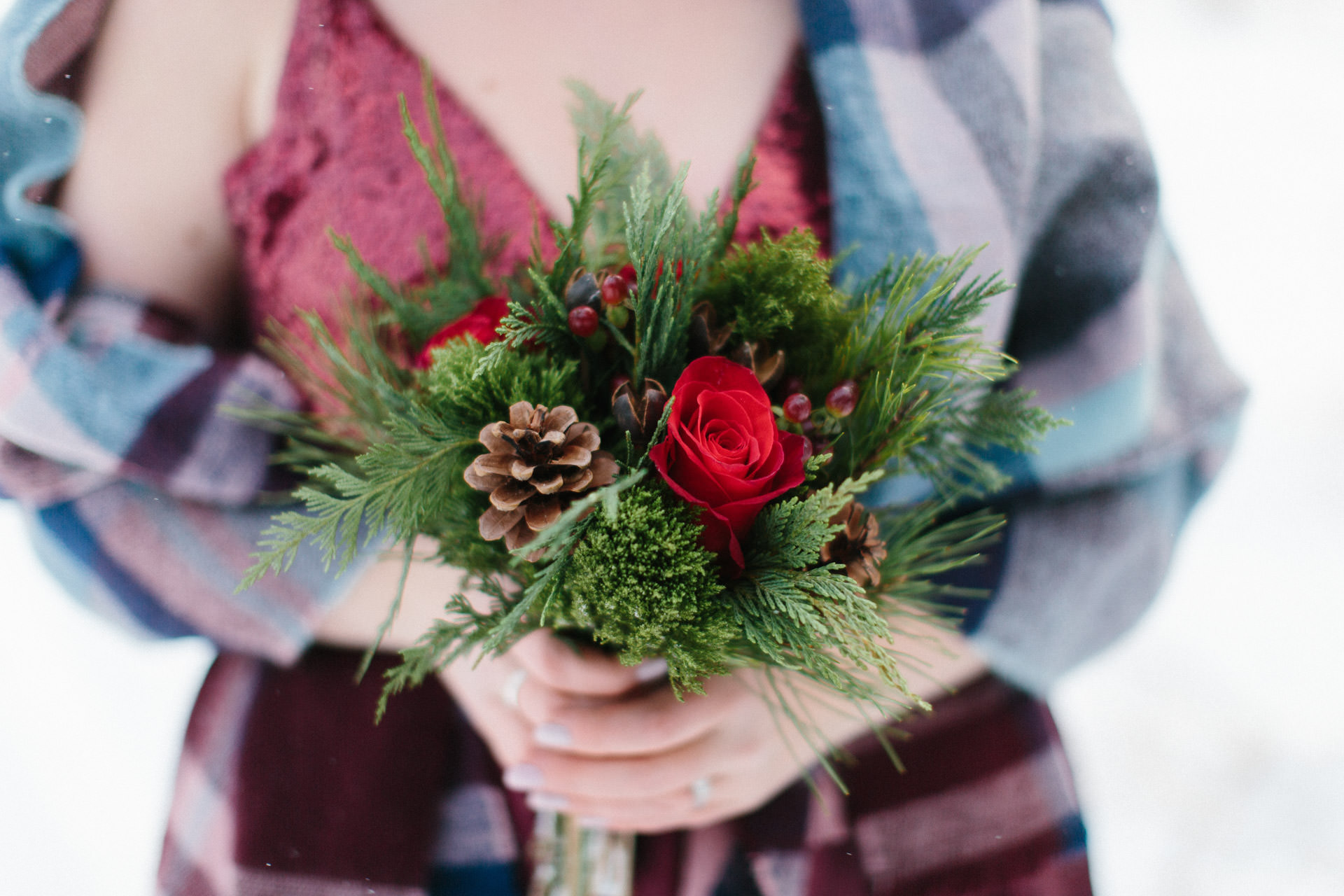 Bride holding winter bouquet with greens and red roses