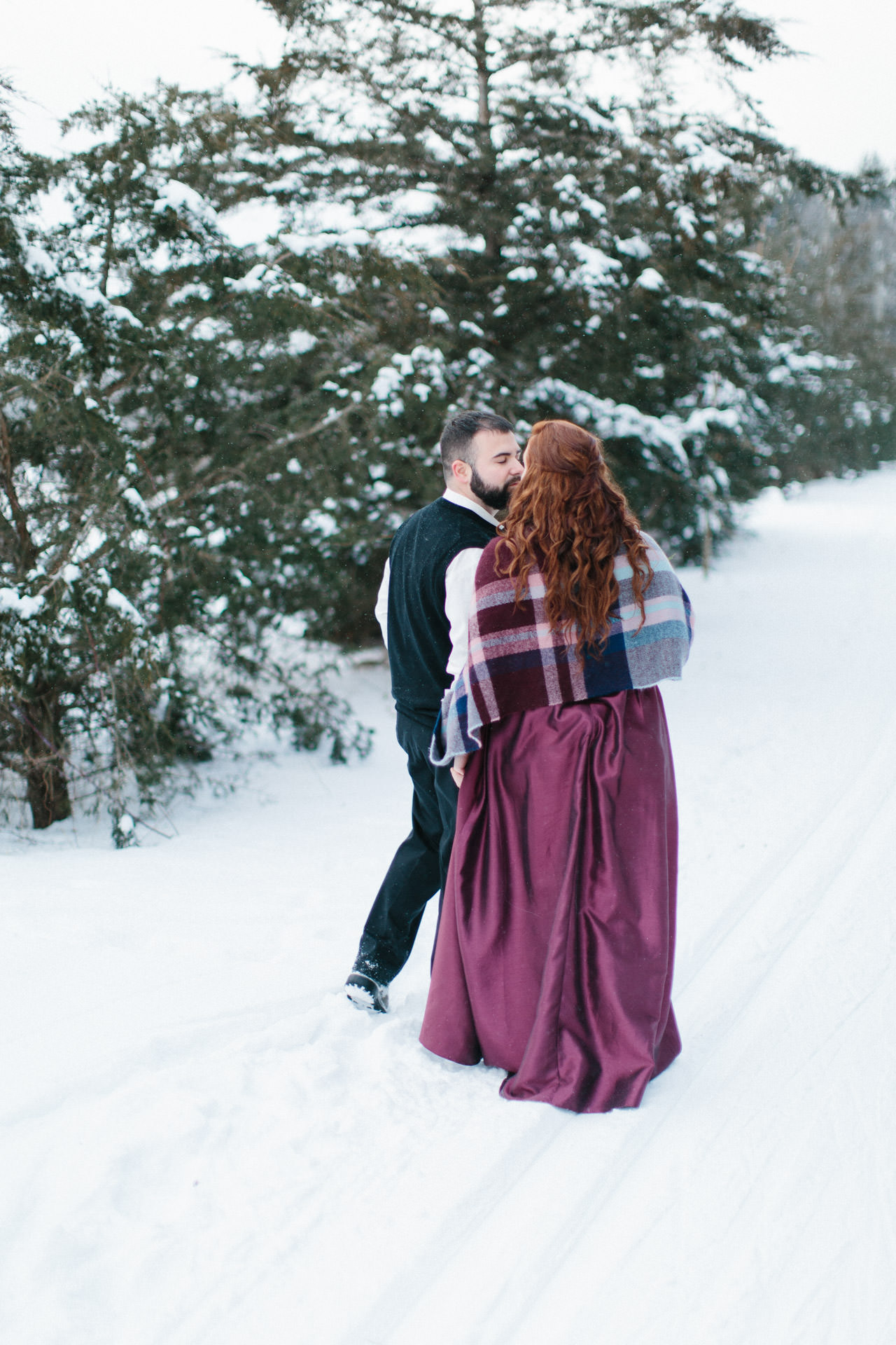 Bride and groom walking in snow and pausing for a kiss